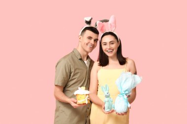 Paskalya pastası, tavşan kulağı, hediye ve pembe arka planda oyuncak tavşan olan mutlu genç çift.