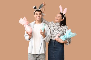 Paskalya hediyeli mutlu genç çift, oyuncak tavşanlar ve bej arka planda tavşan kulakları