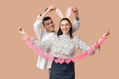 Paskalya çelengi ve bej arka planda tavşan kulaklı mutlu genç çift.