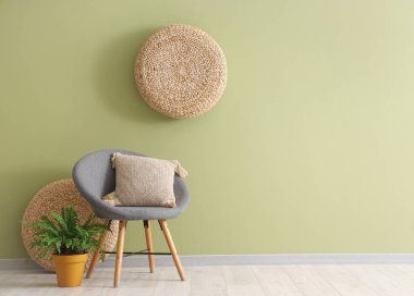 Oturma odasının içinde yeşil duvarın yanında koltuk, yastık ve çiçek var.