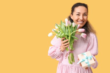 Bir buket güzel lalesi ve sarı arka planda hediye kutusu olan mutlu olgun bir kadın. Uluslararası Kadınlar Günü