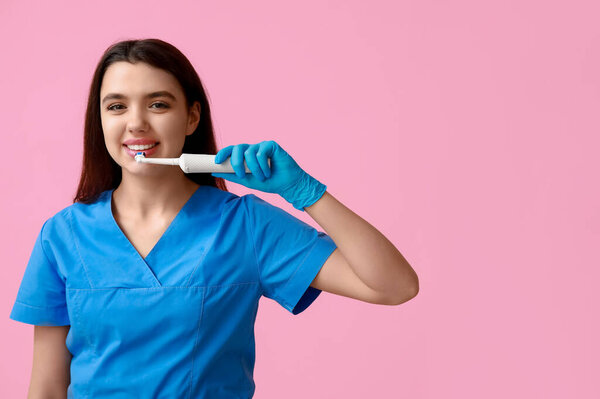 Female dentist with electric toothbrush on pink background. World Dentist Day