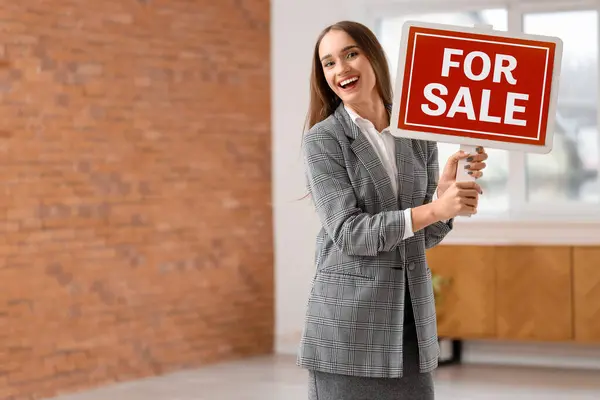 Portrait of female real estate agent with FOR SALE sign in new apartment