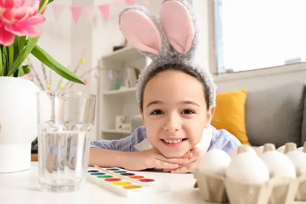可爱的小女孩 长着小兔子的耳朵 坐在餐桌边 一边吃鸡蛋 一边画画 — 图库照片