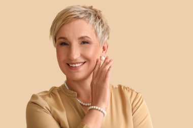 Bej arka planda inci mücevheri olan olgun bir kadın, yakın plan.