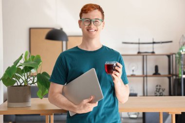 Evde bir bardak meyve suyu ve dizüstü bilgisayarı olan genç bir adam.