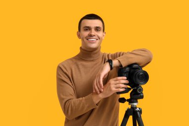 Sarı arka planda modern kameralı bir erkek fotoğrafçı.