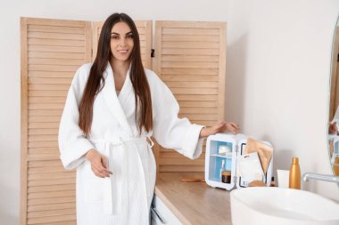 Banyodaki kozmetik ürünleri için küçük buzdolabı olan güzel, mutlu bir kadın.