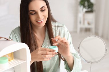 Kozmetik ürünleri için küçük bir buzdolabı olan güzel genç bir kadın yatak odasında krem sürüyor.