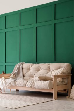 Yeşil duvarın yanında battaniyeli ve yastıklı rahat beyaz kanepe.