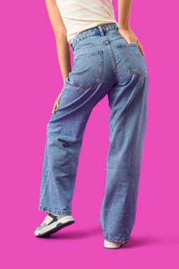 Young woman in stylish jeans on purple background, back view clipart