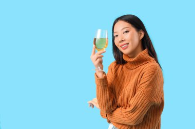 Mavi arka planda bir bardak şarabı olan güzel Asyalı kadın.