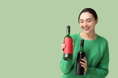 Yeşil arka planda şarap şişeleri olan güzel genç bir kadın.