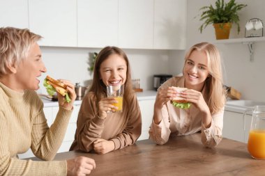 Annesi ve büyükannesiyle mutfakta kahvaltı eden küçük bir kız.