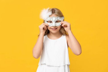 Happy little girl wearing carnival mask on yellow background clipart
