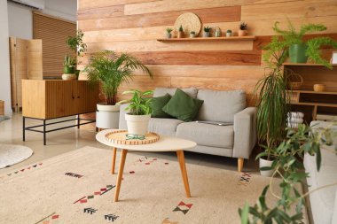 Oturma odasının içinde yeşil bitkiler, kanepe ve masa var.