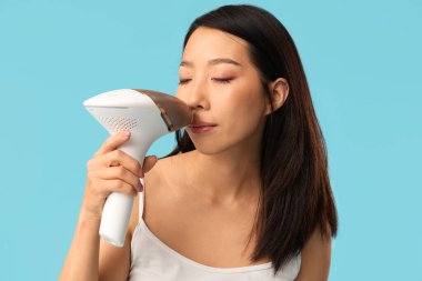 Güzel Asyalı kadın mavi arka planda fotoepilatör kullanıyor.