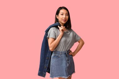 Pembe arka planda şık kot elbiseli güzel, mutlu Asyalı kadın.