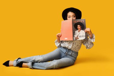 Şık kotlu, dergisi sarı arka planda oturan güzel Asyalı kadın.
