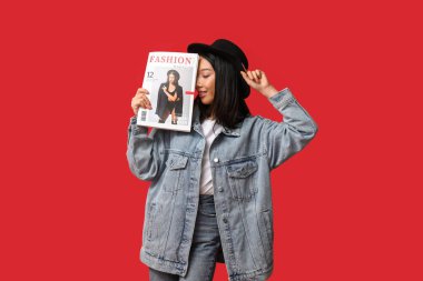 Kırmızı arka planda dergisi olan şık kot elbiseli güzel, genç, mutlu Asyalı kadın.