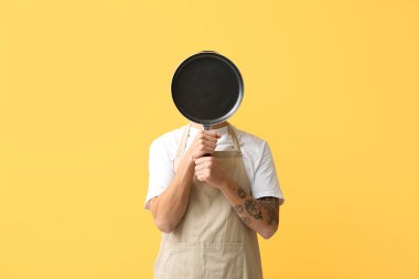 Sarı arka planda tavayla yüzünü kapatan genç adamın portresi.