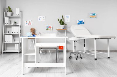 Masası, kanepesi ve çocuk çizimleri olan çocuk doktorunun bürosu.