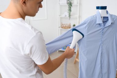 Genç adam evde mavi gömleği buharlaştırıyor, yakın plan.