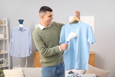 Mutlu genç adam evde buharlı mavi tişört giyiyor.