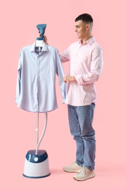 Pembe arka planda modern buharlı ve gömlekli mutlu genç adam.