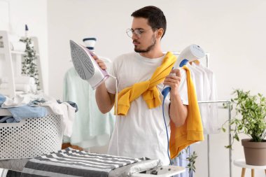 Çamaşır odasında buharlı ve demirli genç adam.