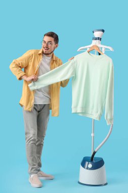 Mavi arka planda modern buharlı ve sweatshirt 'lü mutlu genç adam.