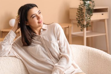 Evdeki oturma odasında rahat bir koltukta oturan güzel, genç ve mutlu bir kadın.