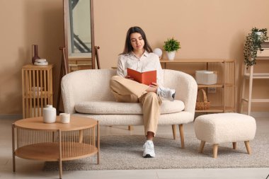 Evdeki oturma odasında rahat bir koltukta oturan güzel, genç ve mutlu bir kadın.