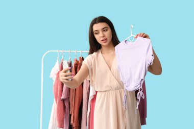 Giysileri askıda, mavi arka planda selfie çeken kadın stilisti.