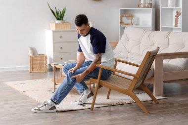 Evdeki sandalyede diz ağrısı çeken genç bir adam.