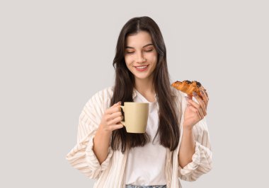 Gri arka planda bir fincan çay ve kruvasanla güzel genç bir kadın.