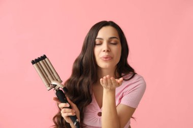 Pembe arka planda saç maşasıyla öpüşen güzel genç bir kadın.