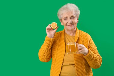 Yeşil arka planda limonlu ve cam fincanlı yaşlı kadın.