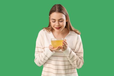 Yeşil arka planda cam bardak limon çayı olan genç bir kadın.