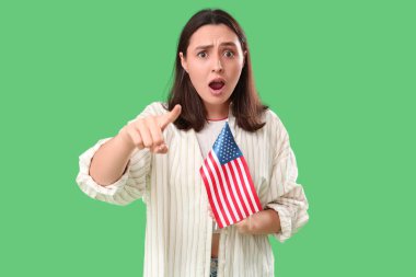 Shocked young woman with USA flag pointing at viewer on green background. Accusation concept clipart