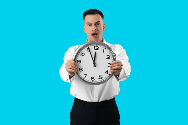 Stressed businessman with clock on blue background. Deadline concept