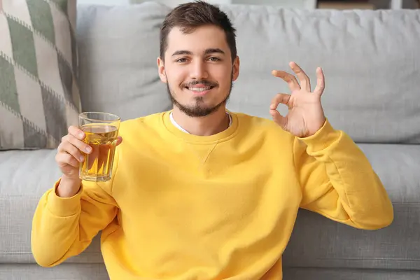 Young man with glass of juice showing OK at home