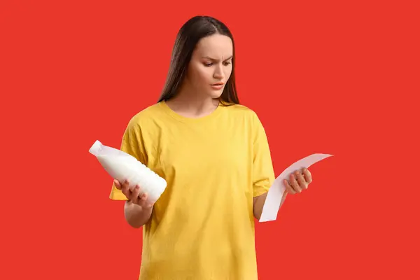 Young woman with milk and store receipt on red background. Price rise concept