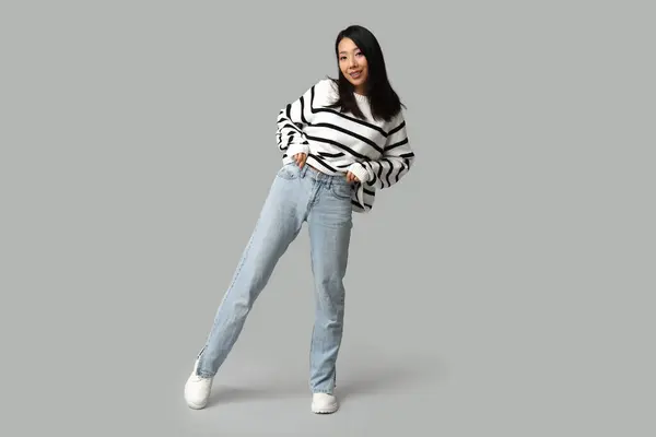 美しい若い幸せなアジアの女性 スタイリッシュなジーンズで灰色の背景 — ストック写真