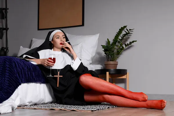 stock image Naughty nun with glass of wine smoking cigarette in bedroom