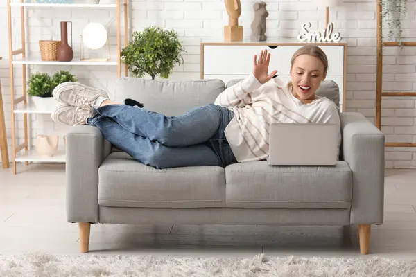 stock image Beautiful young happy woman with laptop lying on comfortable sofa and video chatting in living room at home