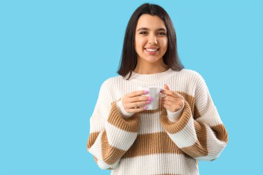 Mavi arka planda bir fincan çayı olan genç bir kadın.