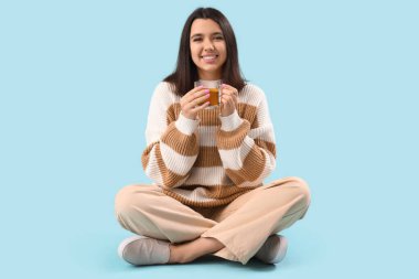 Mavi arka planda oturan cam fincanlı genç bayan.