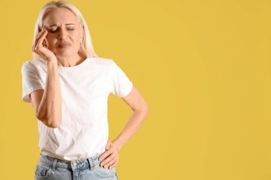 Sarı arka planda baş ağrısı çeken olgun bir kadın.