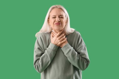 Mature woman suffering from sore throat on green background clipart